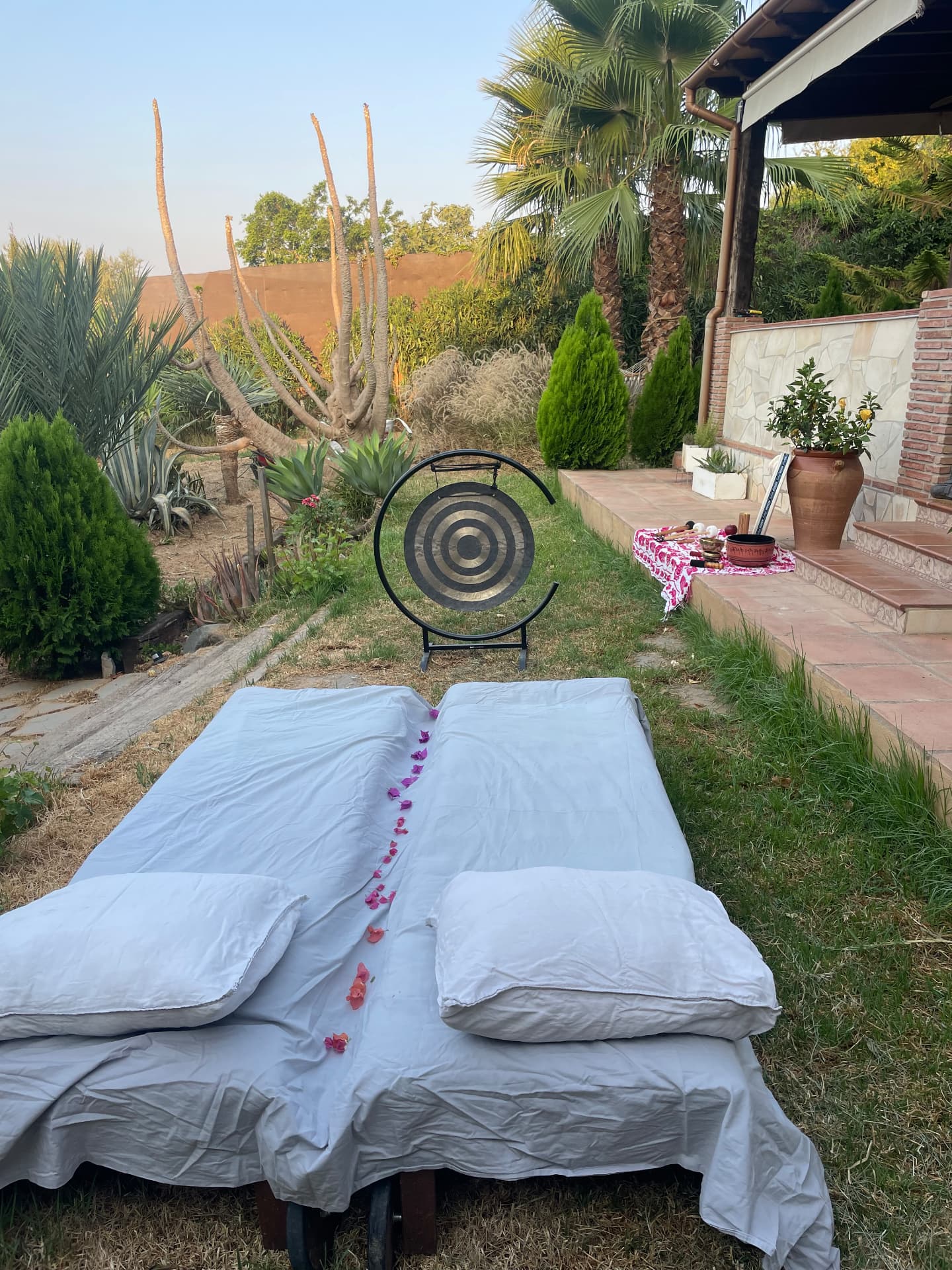Gong and singing bowls set up beside a bed of cushions in the garden